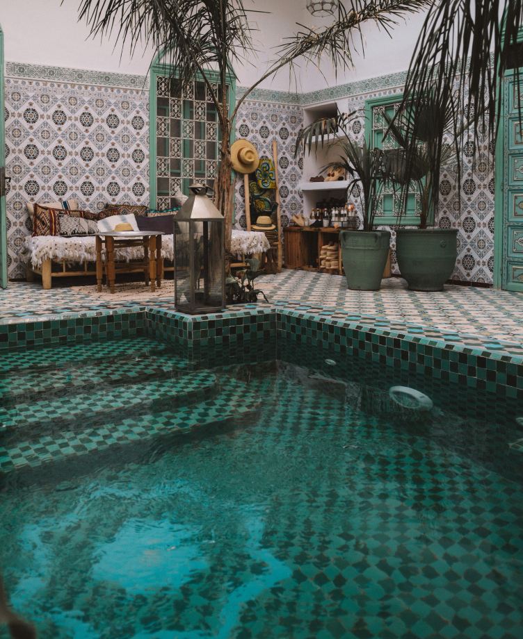 A green-tiled plunge pool in a riad courtyard with plants and a seating area