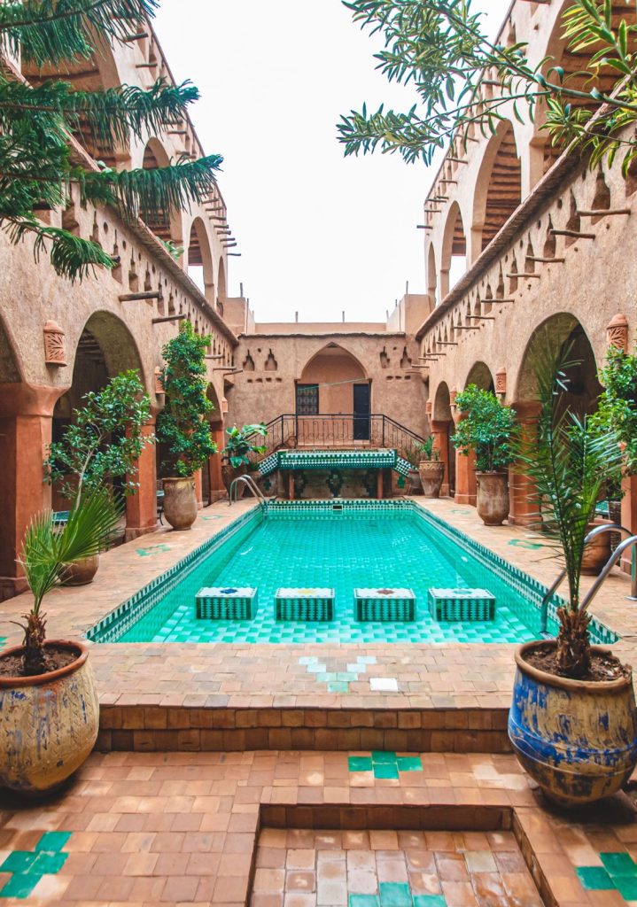 Arcaded riad courtyard with a long turquoise pool, tiled floor and potted trees