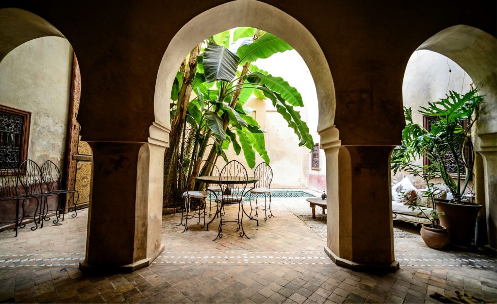 A table and iron chairs under a horseshoe arch, banana leaves behind