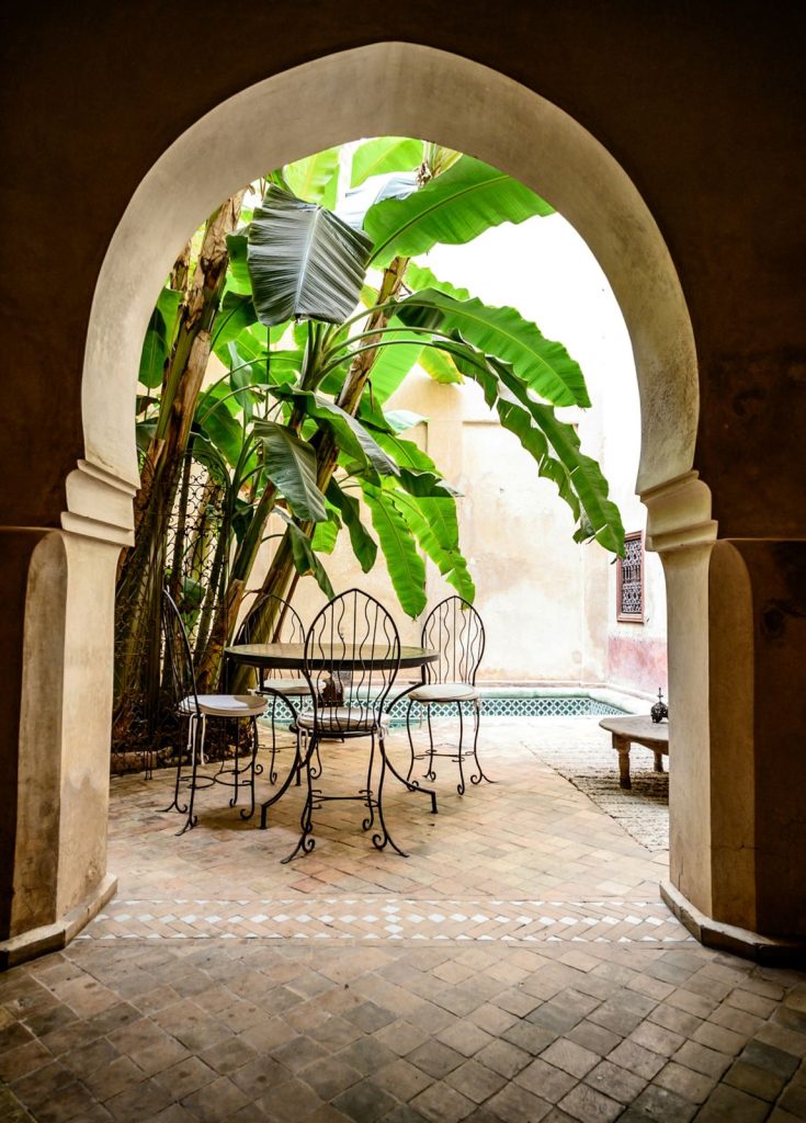 Horseshoe arches opening onto a shaded courtyard with a table and banana plants