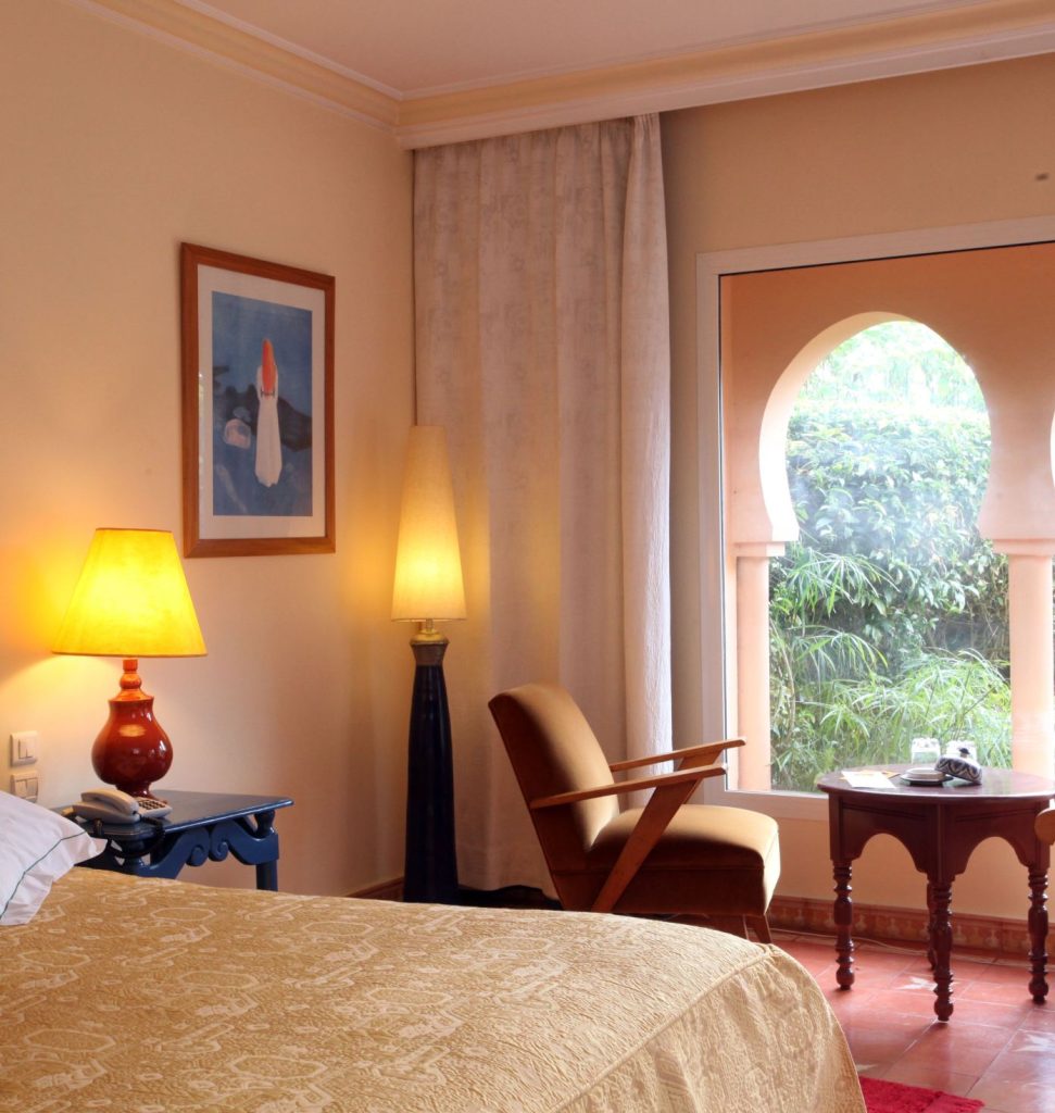 A warm-lit bedroom with arched windows, an armchair and bedside lamps