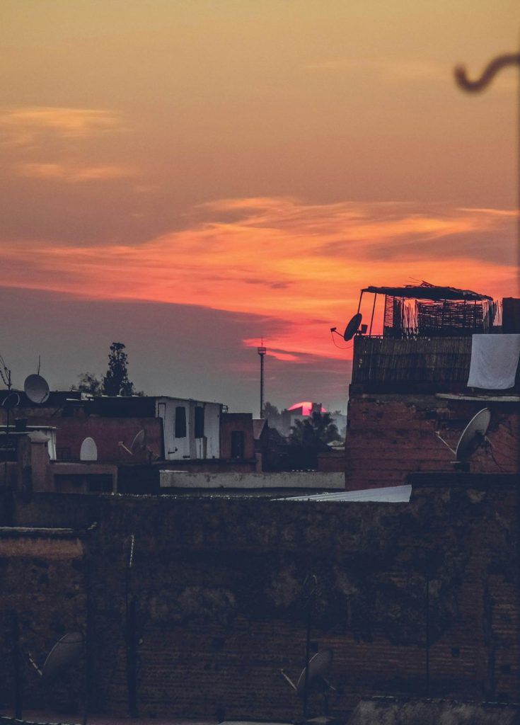 Rooftops and a street lamp in silhouette against an orange sunset sky